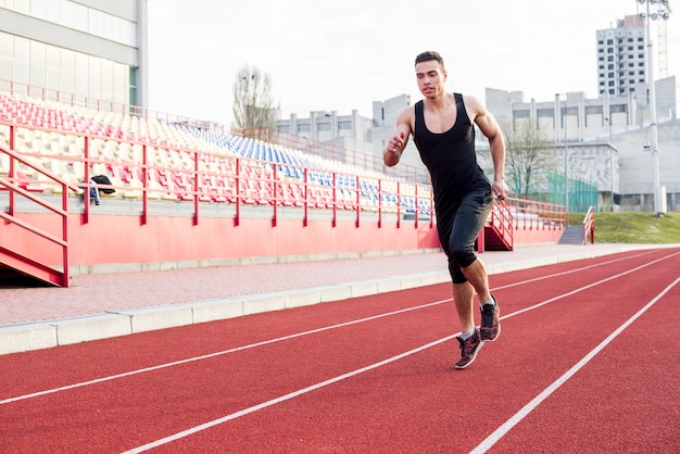 Retrato de fitness joven atleta masculino corriendo en la pista de carreras en el estadio