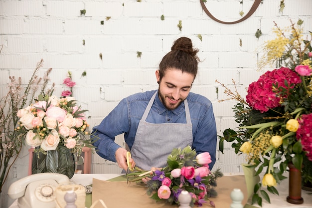 Foto gratuita retrato de un florista masculino envolviendo el ramo de flores en la floristería