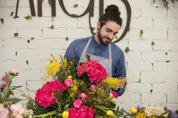 Retrato de un florista de sexo masculino que arregla la flor de mimosa y hortensia macrophylla creando un ramo