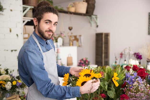 Retrato de una floristería masculina sosteniendo arreglando el ramo de flores mirando a la cámara