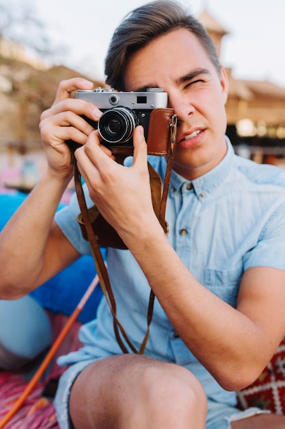Retrato de fotógrafo elegante en camisa de mezclilla azul claro de moda tomando fotos sobre fondo borroso