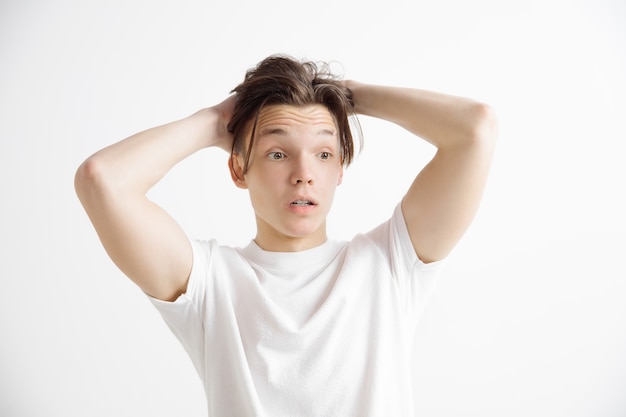 Retrato frontal de medio cuerpo masculino atractivo sobre fondo gris de estudio. Joven sorprendido emocional de pie con la boca abierta. Las emociones humanas, el concepto de expresión facial.