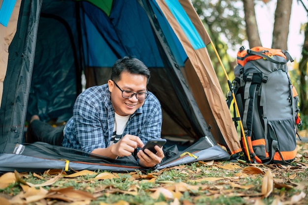 Retrato de gafas de hombre viajero asiático feliz acostado en una tienda de campaña acampar al aire libre y concepto de estilo de vida