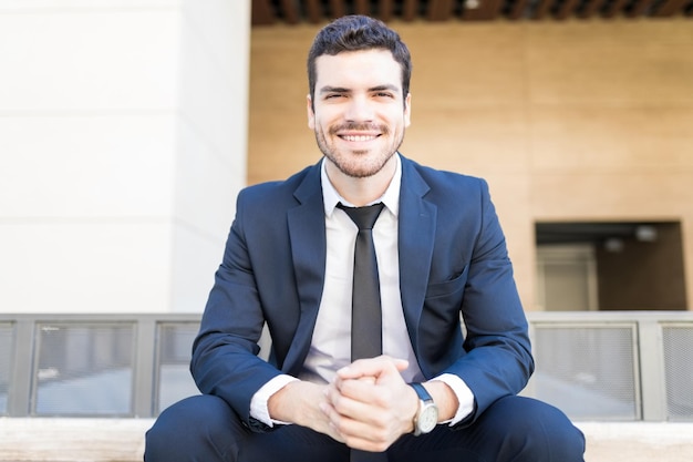 Foto gratuita retrato de un gerente corporativo sonriente sentado con las manos entrelazadas fuera de la oficina