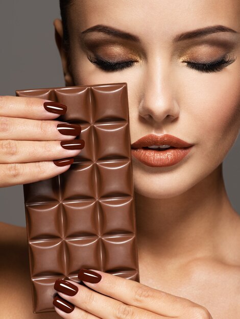 Retrato de glamour Hermosa mujer con uñas marrones tiene barra de chocolate