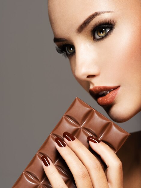 Retrato de glamour Hermosa mujer con uñas marrones tiene barra de chocolate