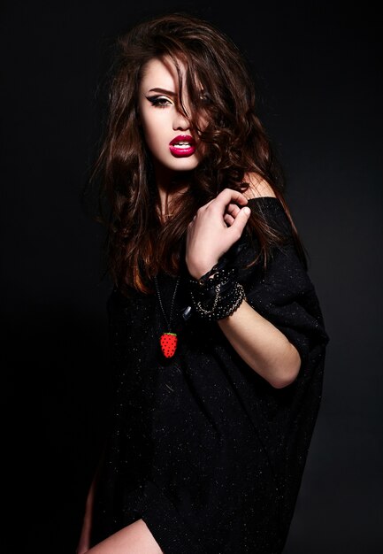 Retrato de glamour de hermosa sexy elegante caucásica joven morena modelo en tela negra con maquillaje brillante con accesorios con piel limpia perfecta con cabello rizado sano con labios rojos