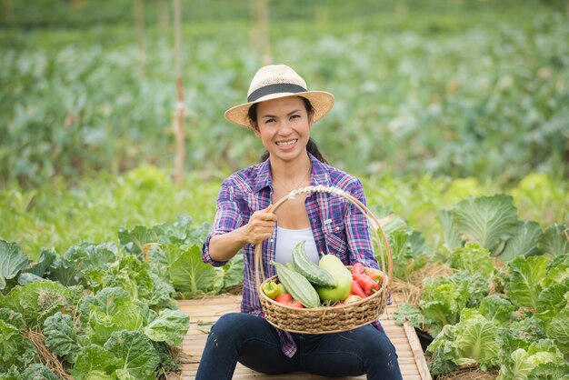 Retrato del granjero de sexo femenino feliz que sostiene una cesta de verduras en la granja