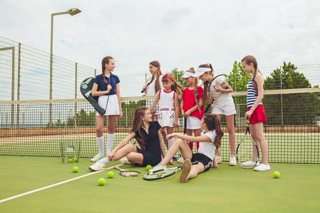 Retrato de un grupo de chicas como tenistas sosteniendo la raqueta de tenis contra la hierba verde de la cancha al aire libre