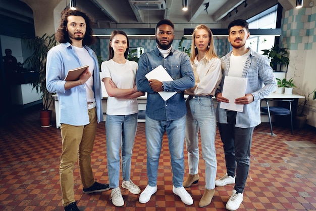 Retrato de grupo de cinco diversos colegas jóvenes de pie en una fila en la oficina