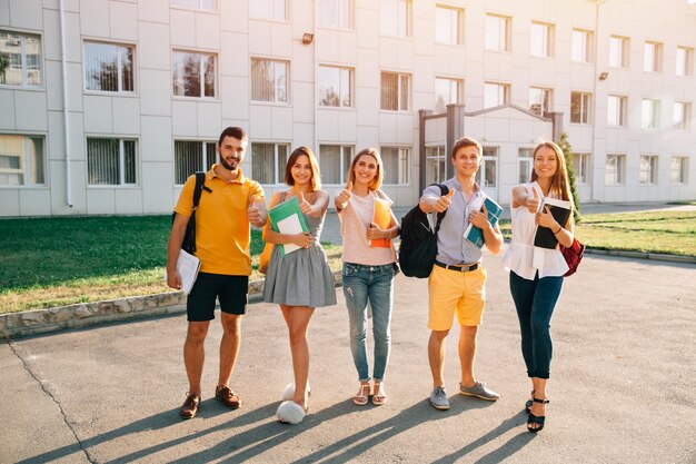 Retrato de un grupo de estudiantes felices en traje casual con libros mostrando los pulgares para arriba