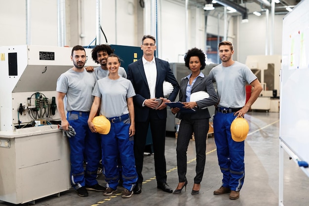 Retrato de un grupo de ingenieros y gerentes corporativos parados en una fábrica y mirando a la cámara