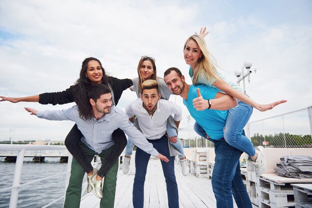 Retrato de un grupo de jóvenes sentados en el borde del muelle, al aire libre en la naturaleza. Amigos disfrutando de un juego en el lago.