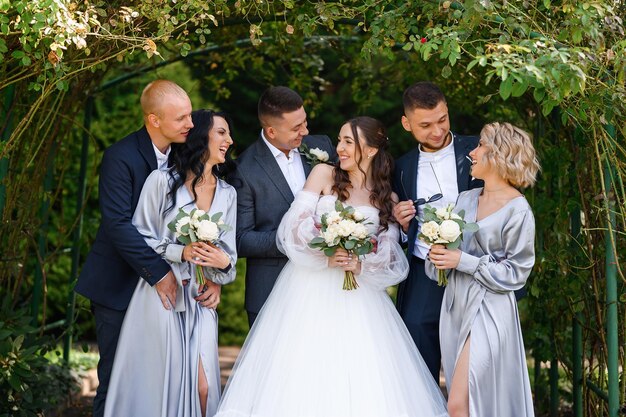 Retrato de grupo de parejas novia con novio y damas de honor con padrinos de boda posando en el jardín cerca del arco sonriendo mirándose el uno al otro Celebración del día de la boda ceremonia al aire libre