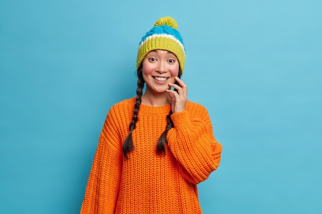 Retrato de guapa chica milenaria asiática con dos coletas toques la cara suavemente tiene las mejillas rojas de las heladas sonríe ampliamente