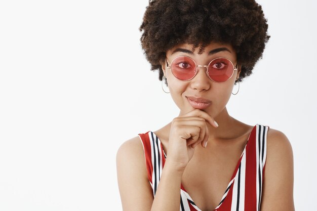 Retrato de guapo afroamericano de moda con gafas de sol, sosteniendo la mano en la barbilla y sonriendo, pensando, gustando concepto interesante