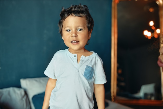 Retrato de guapo alegre niño de piel oscura jugando solo en casa, mirando al frente con sonrisa alegre.