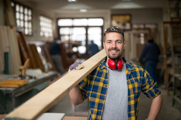 Retrato de guapo carpintero sonriente con material de madera en el taller