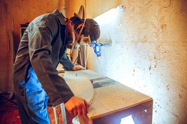 Retrato de guapo carpintero trabajando con patines de madera en el taller, vista de perfil