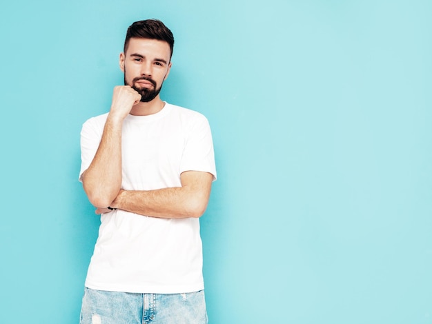 Retrato de guapo confiado con estilo hipster lambersexual modelMan vestido con camiseta blanca y jeans Moda hombre aislado en la pared azul en el estudio