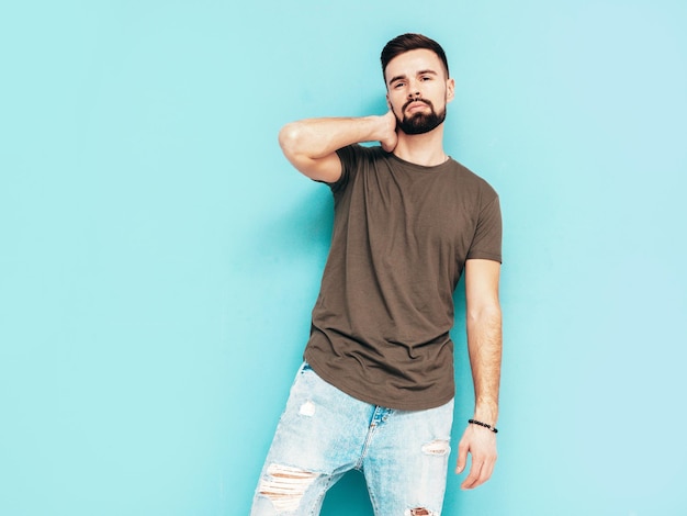 Retrato de guapo confiado con estilo hipster lambersexual modelMan vestido con camiseta y jeans Moda hombre aislado en la pared azul en el estudio