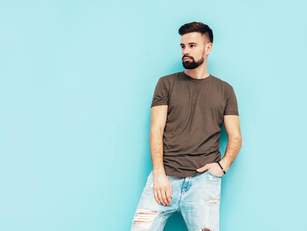 Retrato de guapo confiado con estilo hipster lambersexual modelMan vestido con camiseta y jeans Moda hombre aislado en la pared azul en el estudio