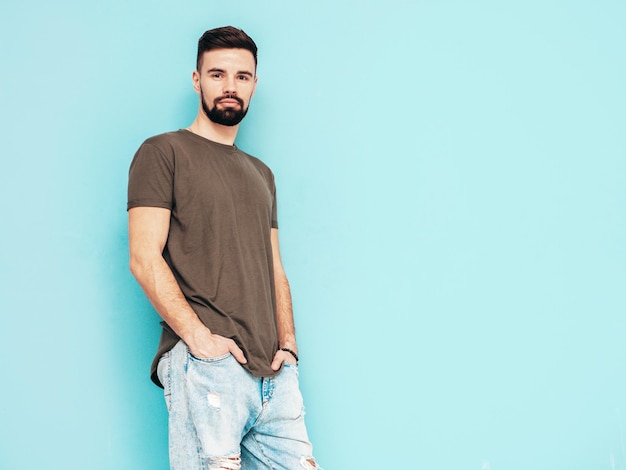 Retrato de guapo confiado con estilo hipster lambersexual modelMan vestido con camiseta y jeans Moda hombre aislado en la pared azul en el estudio