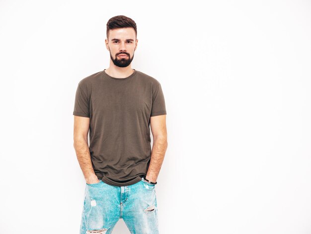 Retrato de guapo confiado con estilo hipster lambersexual modelMan vestido con camiseta y jeans Moda hombre aislado en la pared blanca en el estudio