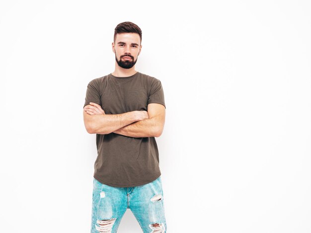 Retrato de guapo confiado con estilo hipster lambersexual modelMan vestido con camiseta y jeans Moda hombre aislado en la pared blanca en el estudio