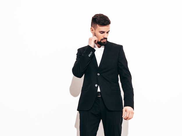 Retrato de guapo confiado con estilo hipster lambersexual modelo Sexy moderno hombre vestido con elegante traje negro Moda hombre posando en estudio cerca de la pared blanca Aislado