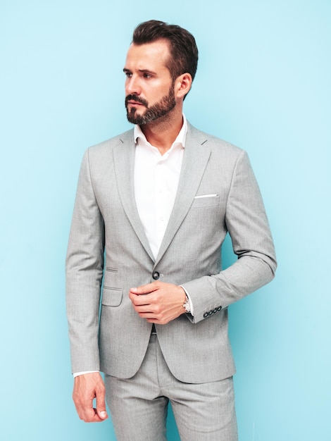 Retrato de guapo confiado con estilo hipster lambersexual modelSexy hombre moderno vestido con traje elegante Hombre de moda posando en el estudio cerca de la pared azul