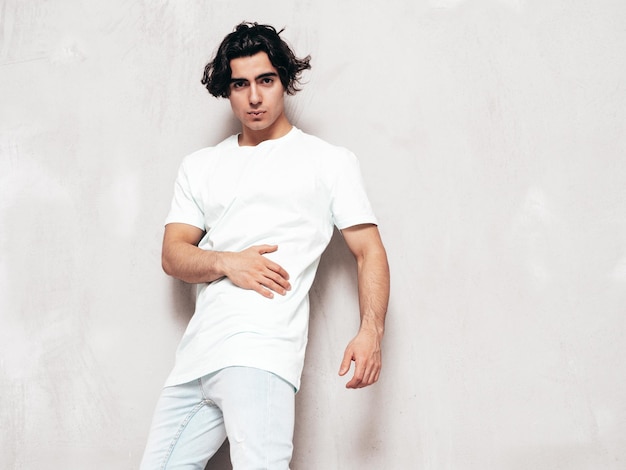 Retrato de guapo confiado con estilo hipster lambersexual modelSexy hombre vestido con camiseta de gran tamaño y jeans Hombre de moda aislado en el estudio Posando cerca de la pared gris