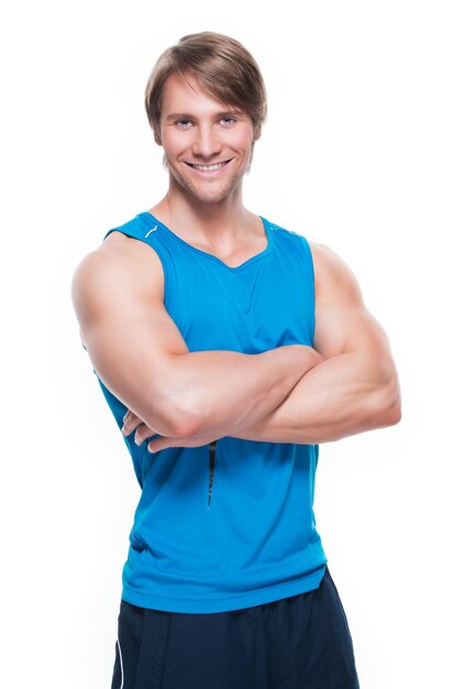 Retrato de guapo deportista feliz en camisa azul posando sobre pared blanca.