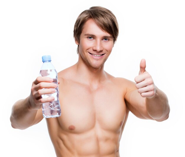 Retrato de guapo deportista musculoso sin camisa tiene agua y muestra los pulgares para arriba signo