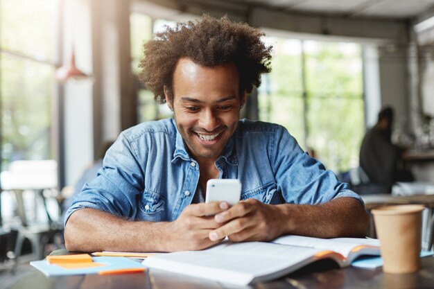 Retrato de guapo estudiante africano de piel oscura con mensaje de mecanografía de smartphone