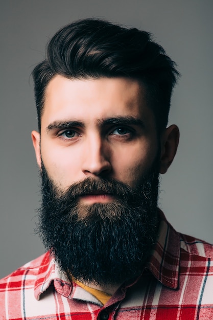 Retrato de guapo joven barbudo aislado en pared gris