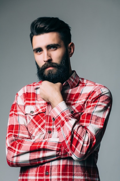 Retrato de guapo joven barbudo con expresión seria sobre pared gris con espacio de copia