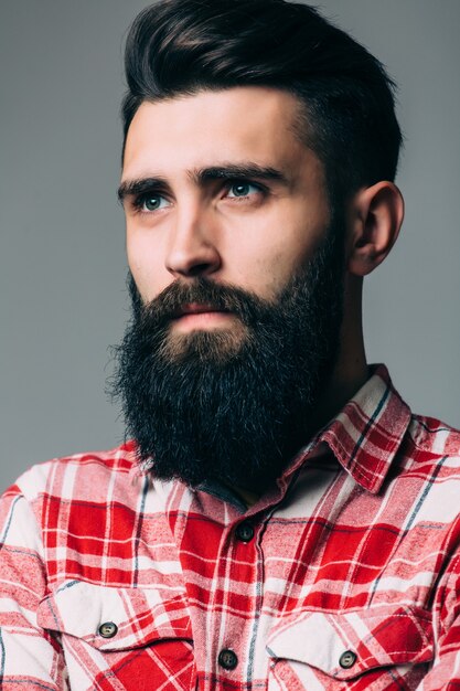 Retrato de guapo joven barbudo con expresión seria sobre pared gris con espacio de copia