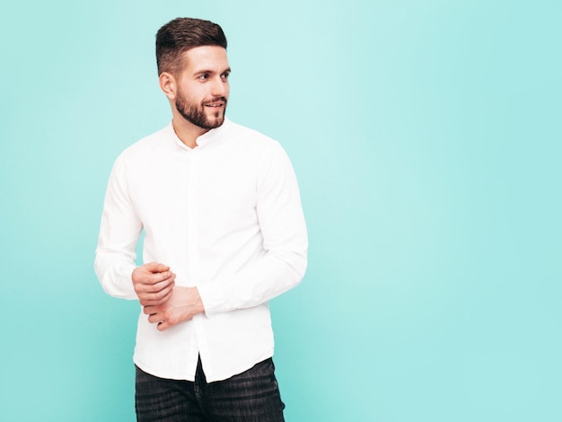 Retrato de guapo modelo confiado Hombre elegante sexy vestido con camisa blanca y jeans Hombre hipster de moda posando junto a la pared azul en el estudio Aislado