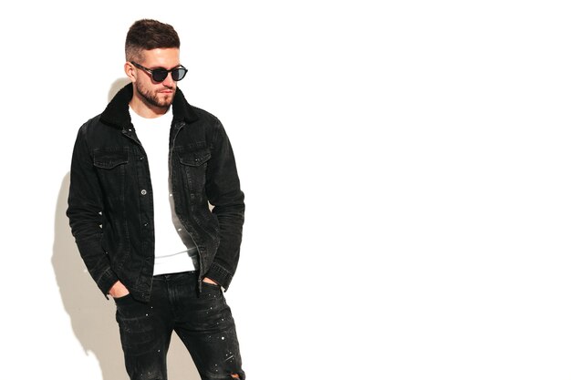 Retrato de guapo modelo confiado Hombre elegante sexy vestido con chaqueta de cuero de motociclista y jeans negros Hombre hipster de moda aislado en blanco en estudio En gafas de sol