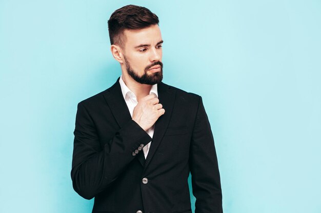 Retrato de guapo modelo lambersexual con estilo hipster con estilo Sexy hombre moderno vestido con elegante traje negro Hombre de moda posando en el estudio cerca de la pared azul