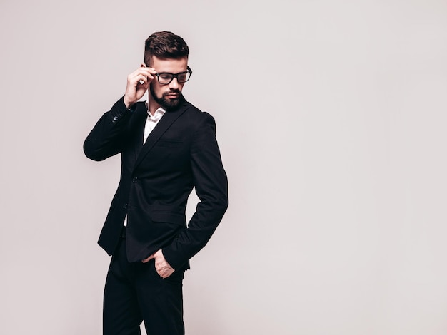 Foto gratuita retrato de guapo modelo lambersexual con estilo hipster seguro hombre moderno sexy vestido con elegante traje negro hombre de moda posando en el estudio cerca de la pared blanca aislado en gris