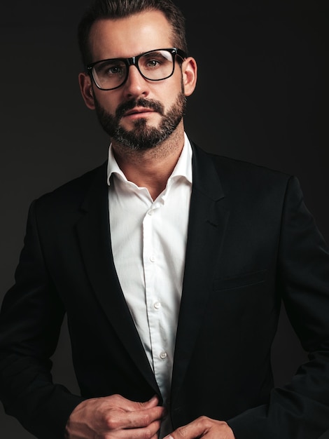 Retrato de guapo modelo lambersexual con estilo hipster sexy hombre moderno vestido con elegante traje negro Hombre de moda posando en el estudio sobre fondo oscuro En espectáculos