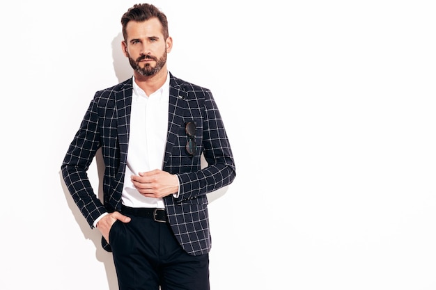 Foto gratuita retrato de guapo modelo lambersexual con estilo inconformista confiado hombre moderno sexy vestido con traje negro elegante hombre de moda posando en el estudio cerca de la pared blanca