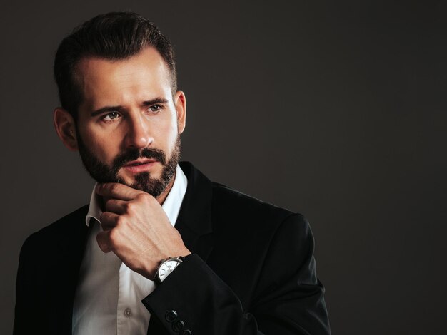 Retrato de guapo modelo lambersexual hipster con estilo seguro Hombre moderno sexy vestido con elegante traje negro Hombre de moda posando en el estudio sobre fondo oscuro