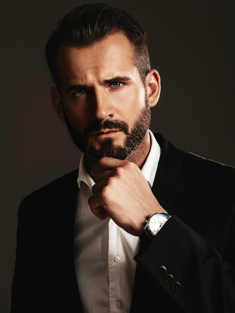 Retrato de guapo modelo lambersexual hipster con estilo seguro Hombre moderno sexy vestido con elegante traje negro Hombre de moda posando en el estudio sobre fondo oscuro