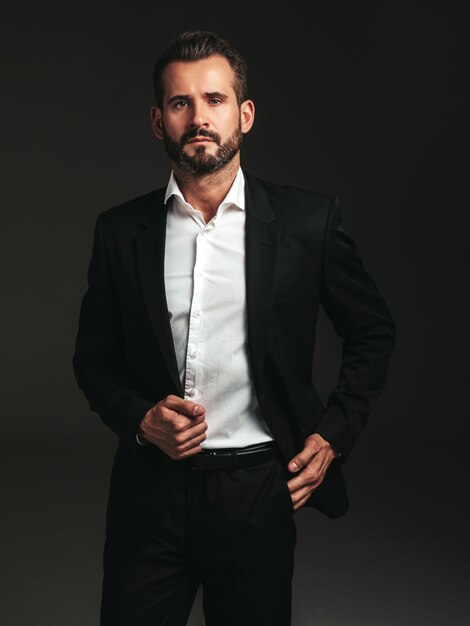 Retrato de guapo modelo lambersexual hipster con estilo seguro Hombre moderno sexy vestido con elegante traje negro Hombre de moda posando en el estudio sobre fondo oscuro