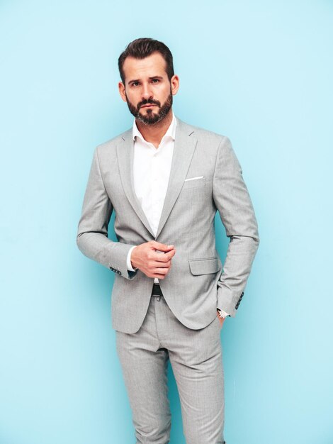 Retrato de guapo modelo lambersexual hipster con estilo seguro Hombre moderno sexy vestido con traje elegante Hombre de moda posando en el estudio cerca de la pared azul Mirando a la cámara