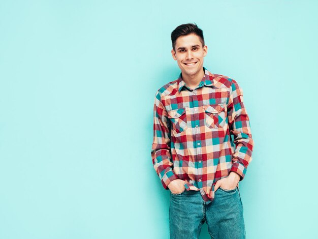 Retrato de guapo modelo sonriente Hombre elegante sexy vestido con camisa a cuadros roja y jeans Hombre hipster de moda posando cerca de azul en el estudio Aislado