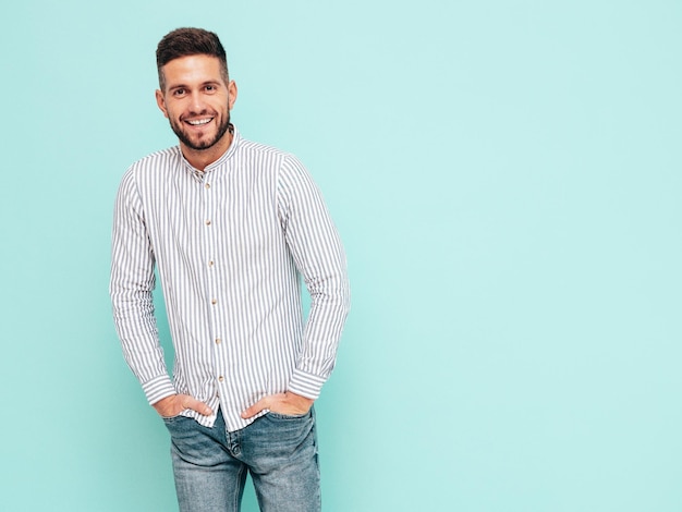 Retrato de guapo modelo sonriente Hombre elegante sexy vestido con camisa y jeans Hombre hipster de moda posando junto a la pared azul en el estudio